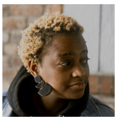 A portrait of a Black woman with short, blond curly hair looking off camera.