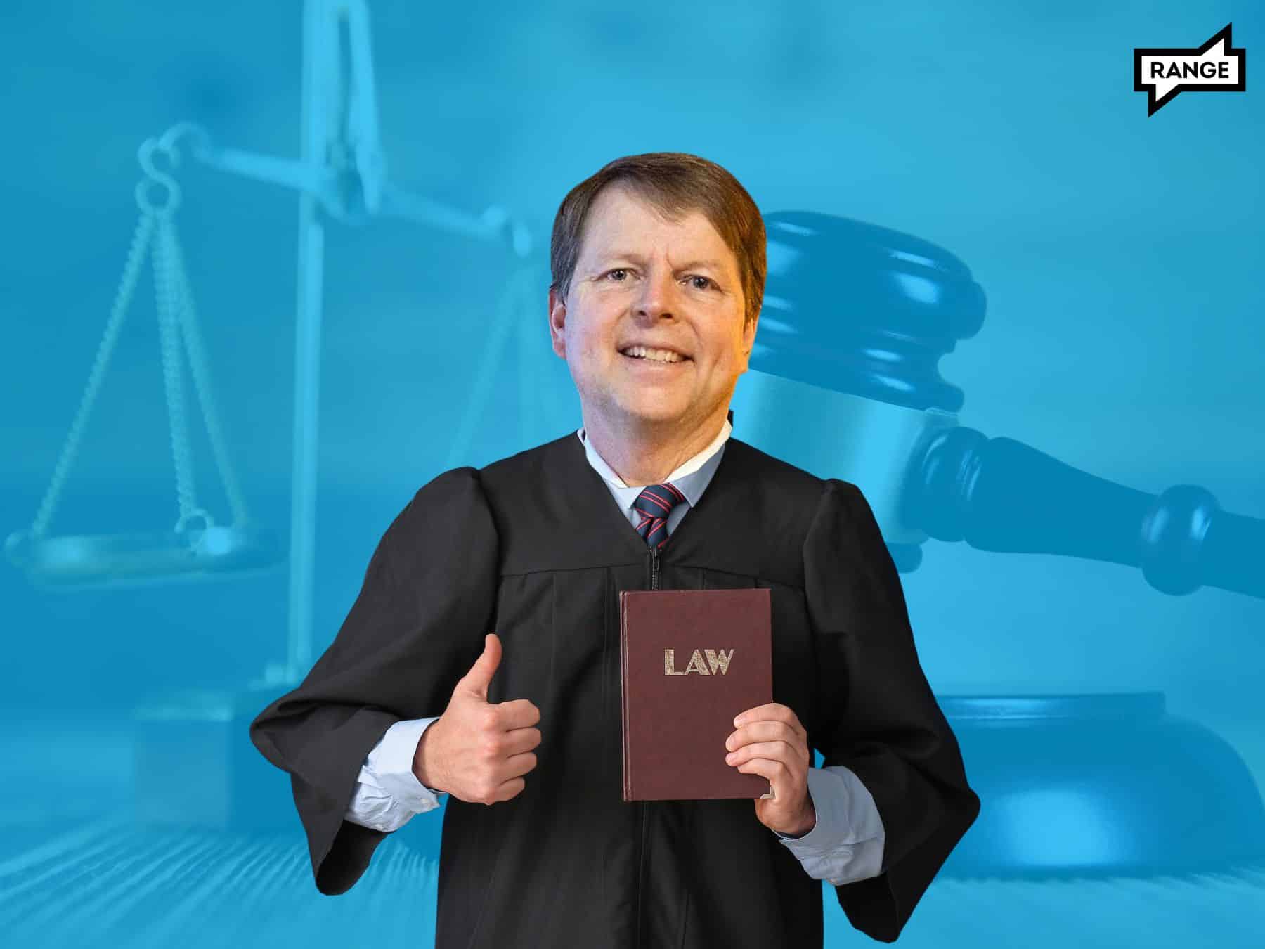 Breean Beggs' head on the body of a white man in black judge's robes with his right thumb up and holding a brown book with "LAW" in gold letters in his left hand. 