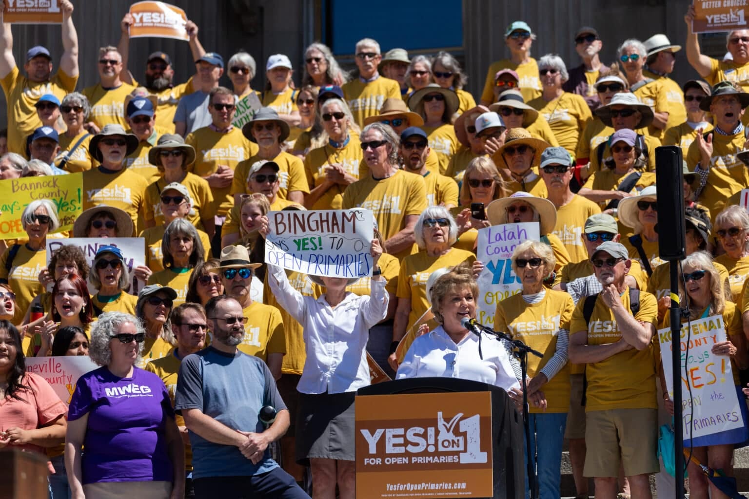 A crowd of supporters of the Idaho open primary initiative — donning mustard yellow t-shirts — stand on the front steps of the Idaho State Capitol Building.